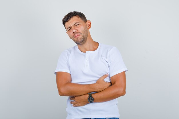 Young man suffering from stomach pain in white t-shirt and looking ill, front view