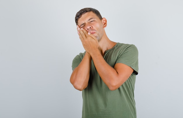 Young man suffering from toothache in army green t-shirt and looking painful, front view.