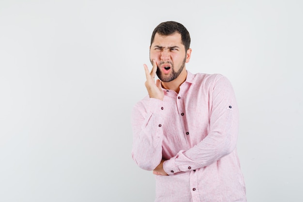 Young man suffering from toothache in pink shirt and looking anxious