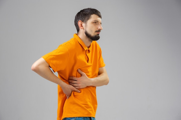 Free photo young man suffers from pain feels sick ill and weakness isolted on wall