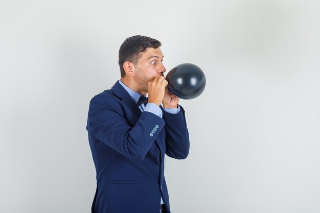 Young man in suit blowing black balloon 