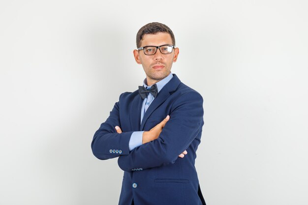 Young man in suit, glasses standing with crossed arms and looking confident