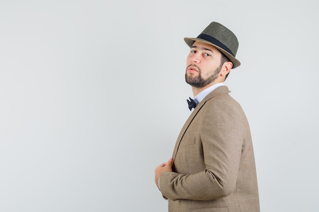 Free photo young man in suit, hat holding his jacket and looking confident .