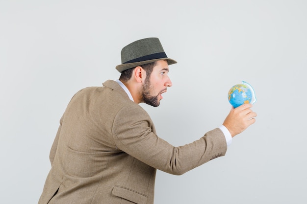 Foto gratuita giovane uomo in tuta, cappello guardando il globo del mondo e guardando concentrato.