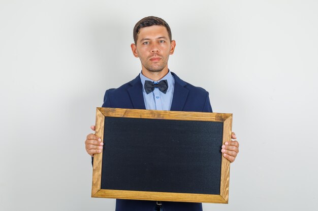 Young man in suit holding blackboard and looking serious 