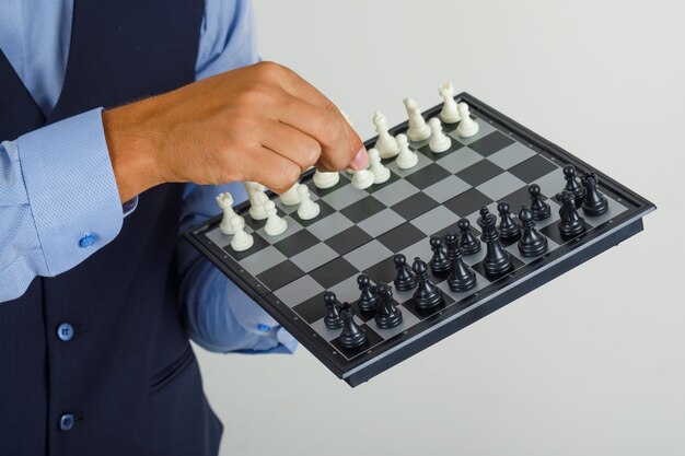 Young man in suit holding chessboard and figure 