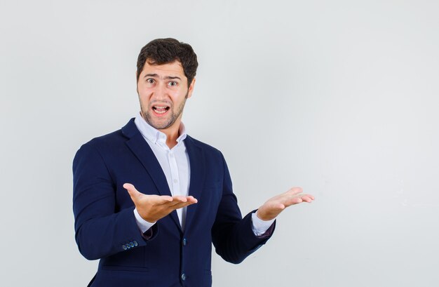 Young man in suit holding hands expressing misunderstanding and looking confused , front view.