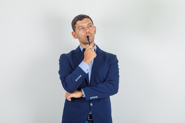 Young man in suit holding pen to his lips and looking pensive 