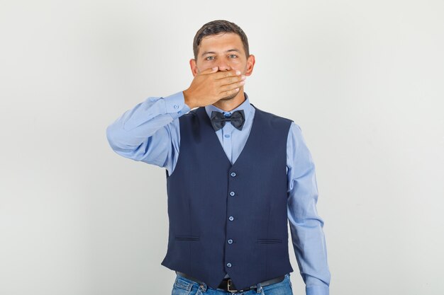 Young man in suit, jeans covering his mouth with hand