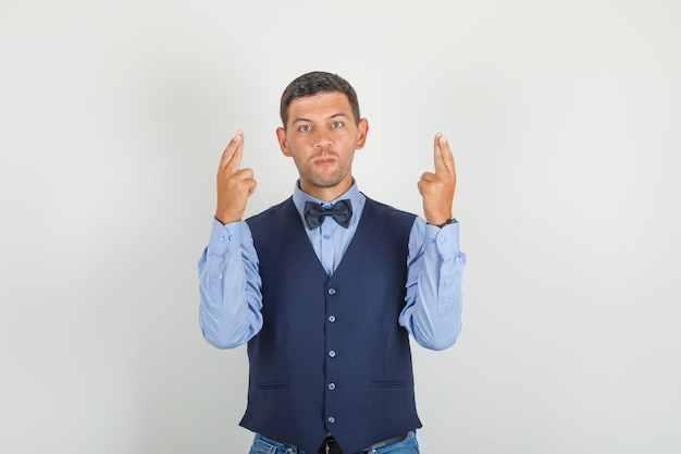 Young man in suit, jeans holding fingers crossed