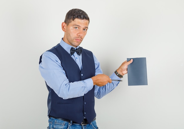 Young man in suit, jeans pointing pen at copybook and looking serious