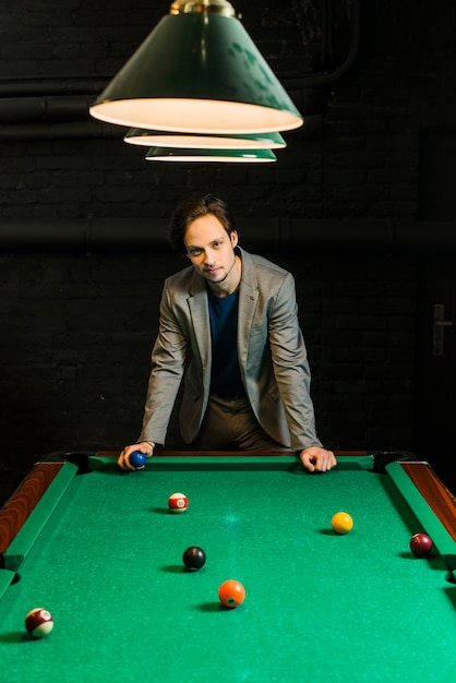 Free photo young man in suit standing behind billiard pool holding ball in club