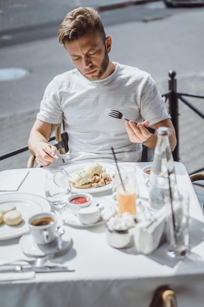 테라스에 있는 여름 카페에서 젊은 남자가 아침을 먹는다