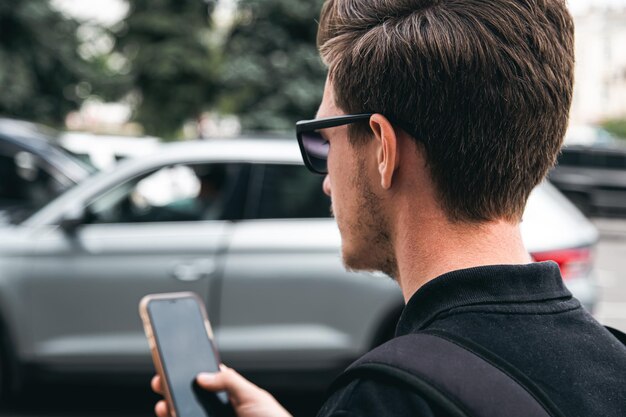 A young man in sunglasses uses a smartphone closeup