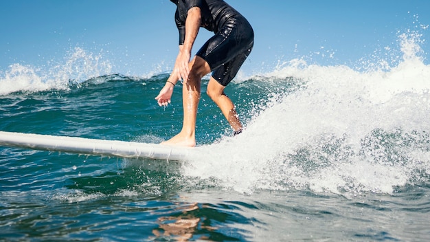 若い男は海の澄んだ水の波をサーフィンします