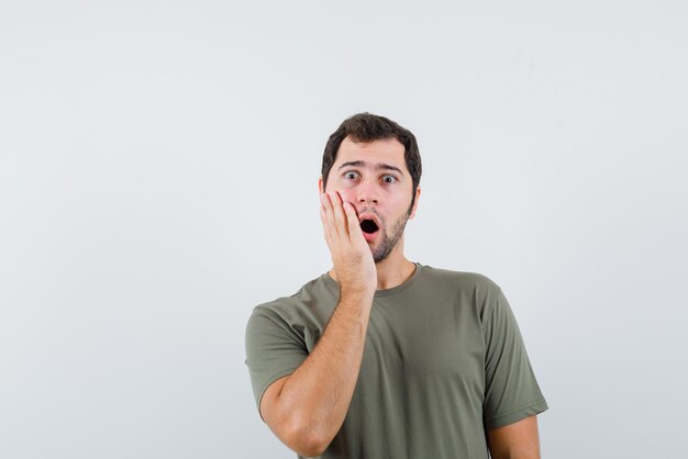 Young man surprises and holding his hands on his face on white background