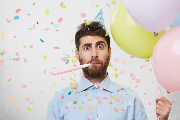 Young man surrounded by confetti holding balloons