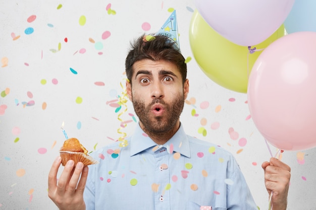 Foto gratuita giovane uomo circondato da coriandoli che tengono cupcake e palloncini