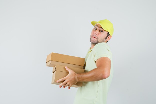 Молодой человек в кепке футболки держит тяжелые картонные коробки