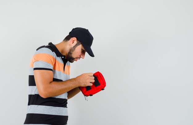 Tシャツを着た若い男、救急箱を開けて不安そうなキャップ。