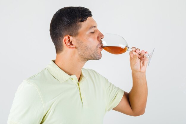 Young man in t-shirt drinking glass of alcohol .