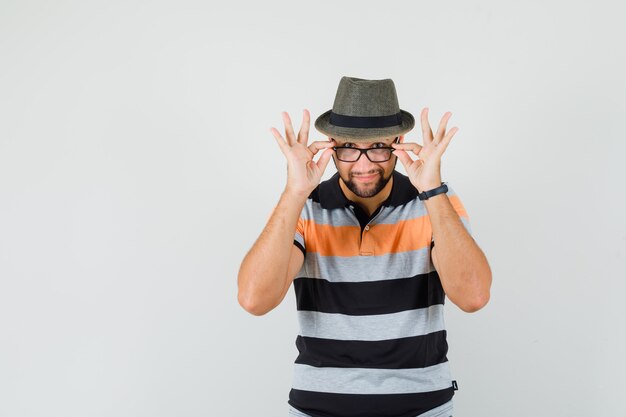 Foto gratuita giovane uomo in t-shirt, cappello guardando sopra gli occhiali e sorridente, vista frontale.