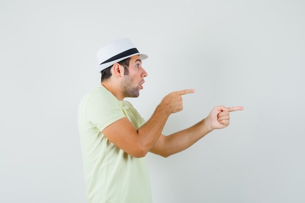 Young man in t-shirt hat pointing to the side and looking focused