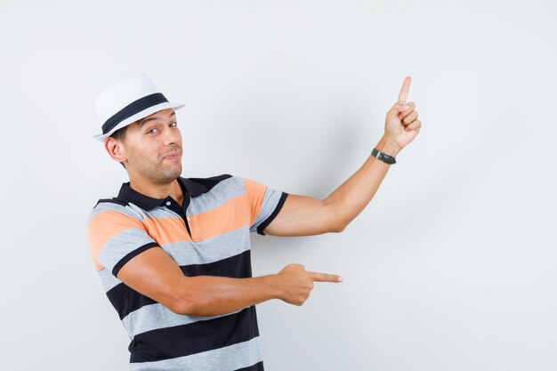 Young man in t-shirt and hat pointing to side and up and looking joyful