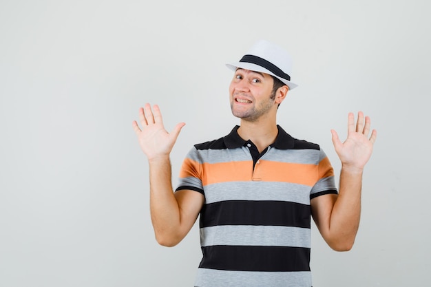 Young man in t-shirt,hat raising hands and looking happy
