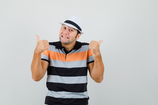 Молодой человек в футболке, шляпе показывает большой палец вверх и выглядит весело