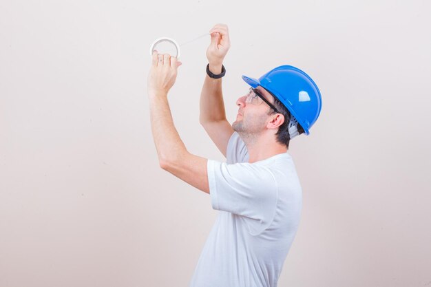 Young man in t-shirt, helmet opening roll of duct tape and looking careful