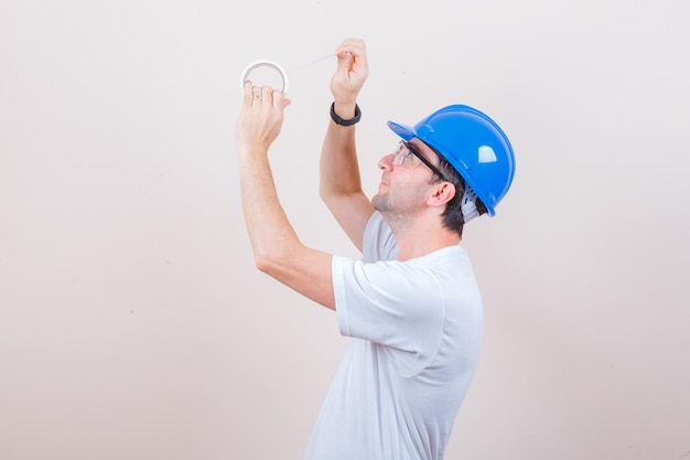 Молодой человек в футболке, шлем, открывающий рулон изоленты и осторожно выглядящий