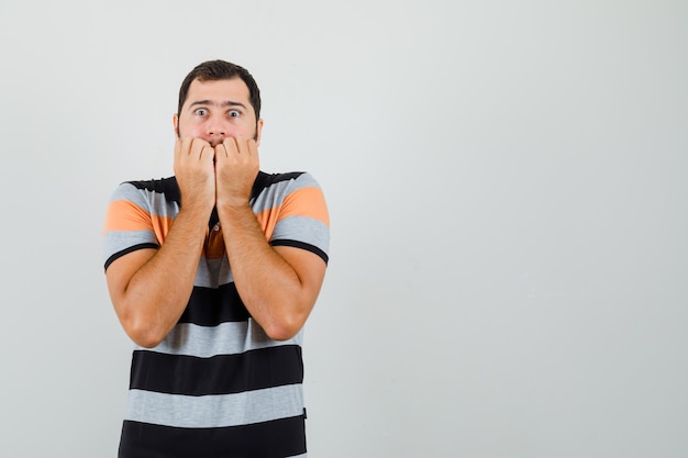 Young man in t-shirt holding hand on his chin and looking excited space for text