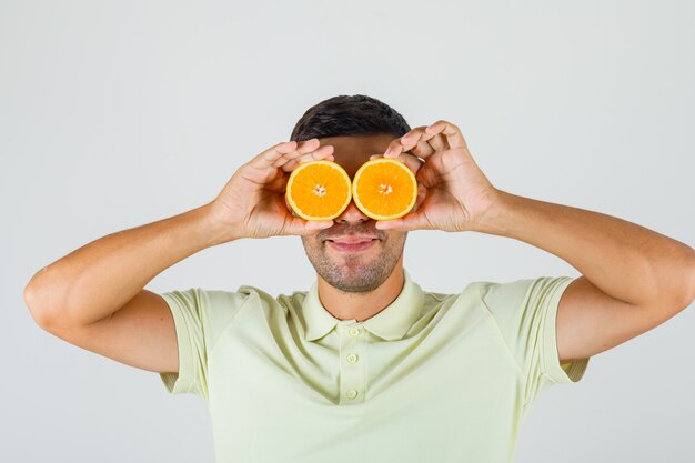 Молодой человек в футболке держит дольки апельсина над глазами