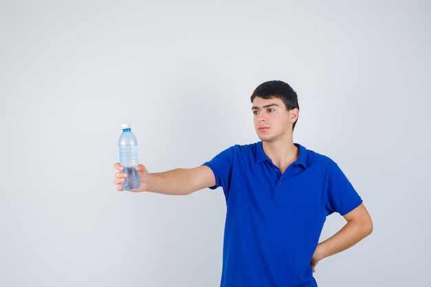 Young man in t-shirt holding plastic bottle in hand and looking confident , front view.
