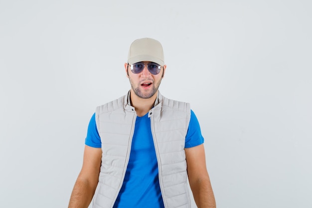 Free photo young man in t-shirt, jacket, cap looking at camera and looking confident , front view.