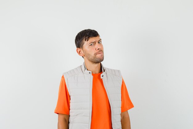 Young man in t-shirt, jacket frowning and looking doubtful , front view.