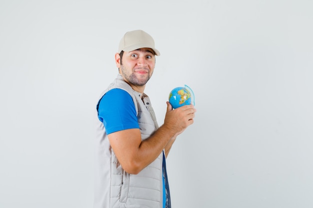 Free photo young man in t-shirt, jacket holding school globe and looking hopeful .