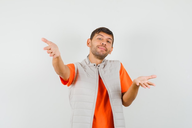 Giovane uomo in t-shirt, giacca che apre le braccia per abbraccio e sembra allegro, vista frontale.