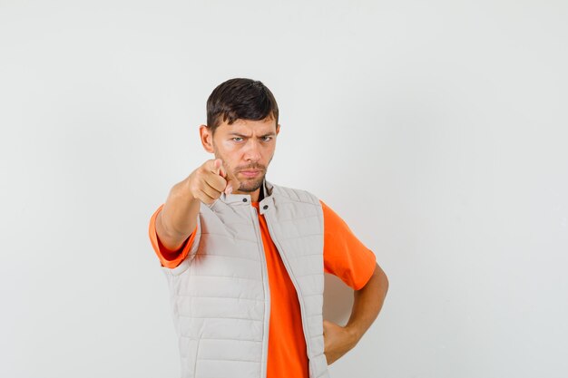 Young man in t-shirt, jacket pointing at camera and looking serious , front view.