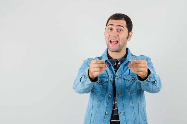 Young man in t-shirt, jacket showing glasses and looking cheery