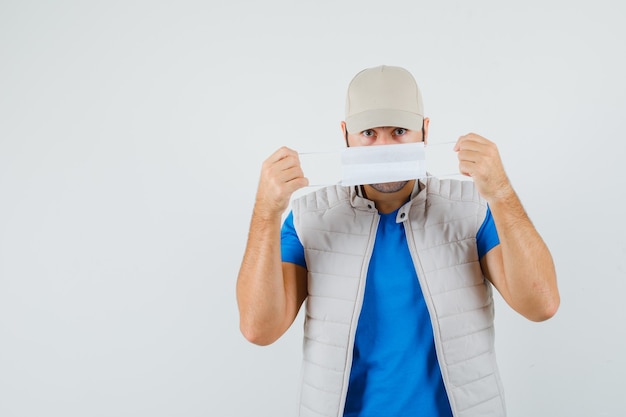 Young man in t-shirt, jacket wearing medical mask and looking careful , front view.