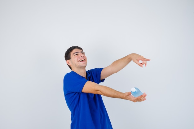 플라스틱 병을 손에 들고 오른쪽을 가리키고 기쁘게 생각하는, 정면도를보고있는 티셔츠에 젊은 남자.