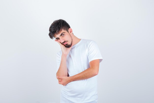 Young man in t-shirt leaning cheek on hand and looking wistful