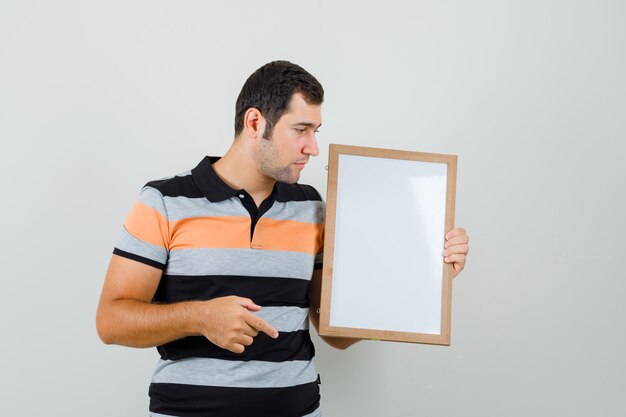 Young man in t-shirt looking at blank frame and looking focused