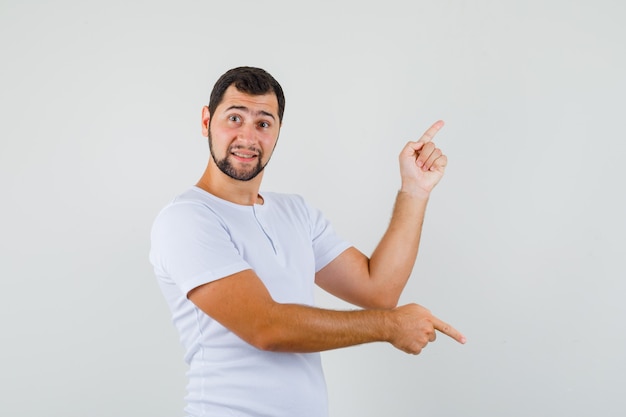 Young man in t-shirt pointing fingers up and down and looking focused , front view.