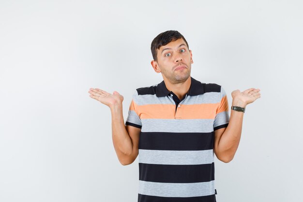 Young man in t-shirt raising palms like holding something and looking confused 