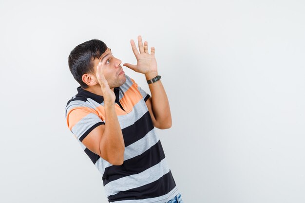 予防的な方法で手のひらを上げて怖がって見えるTシャツの若い男