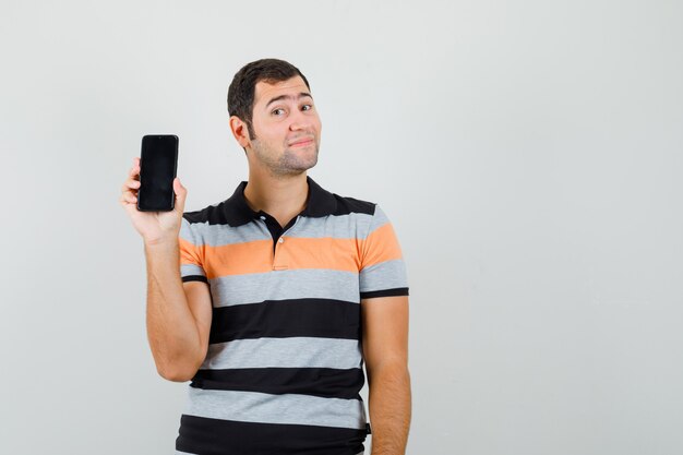 Young man in t-shirt showing his phone and looking satisfied