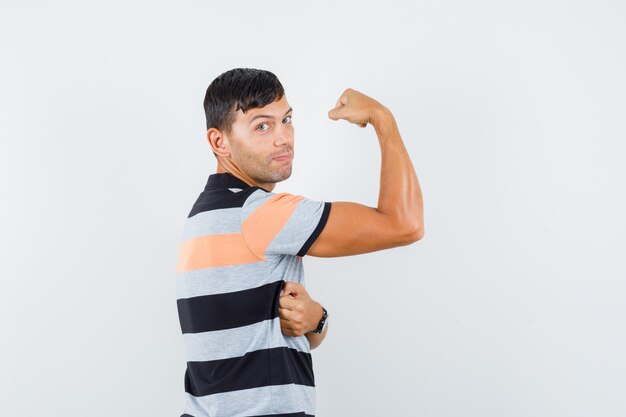 Young man in t-shirt showing muscles of arm and looking strong